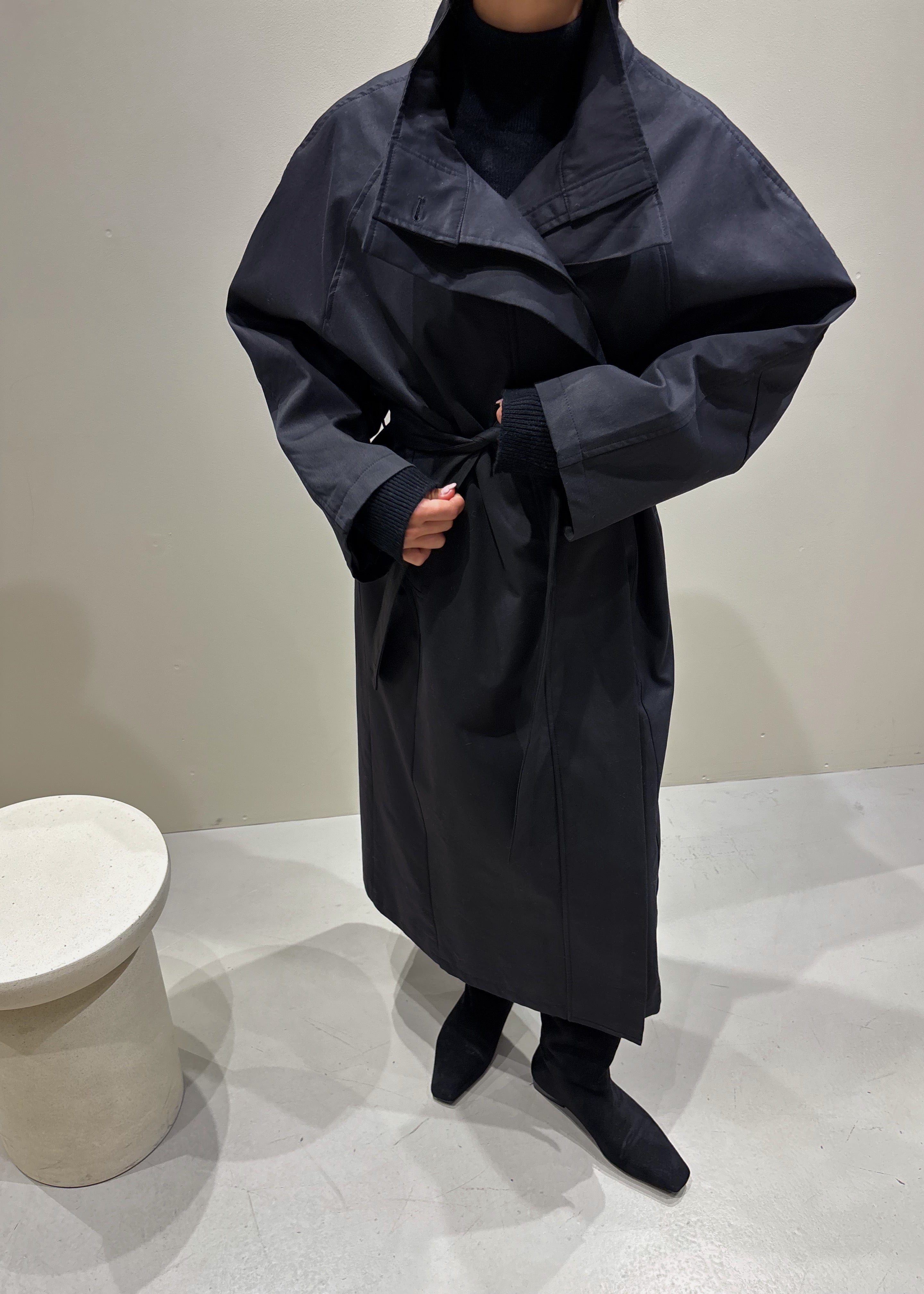 Person wearing a long dark coat in a minimal indoor setting