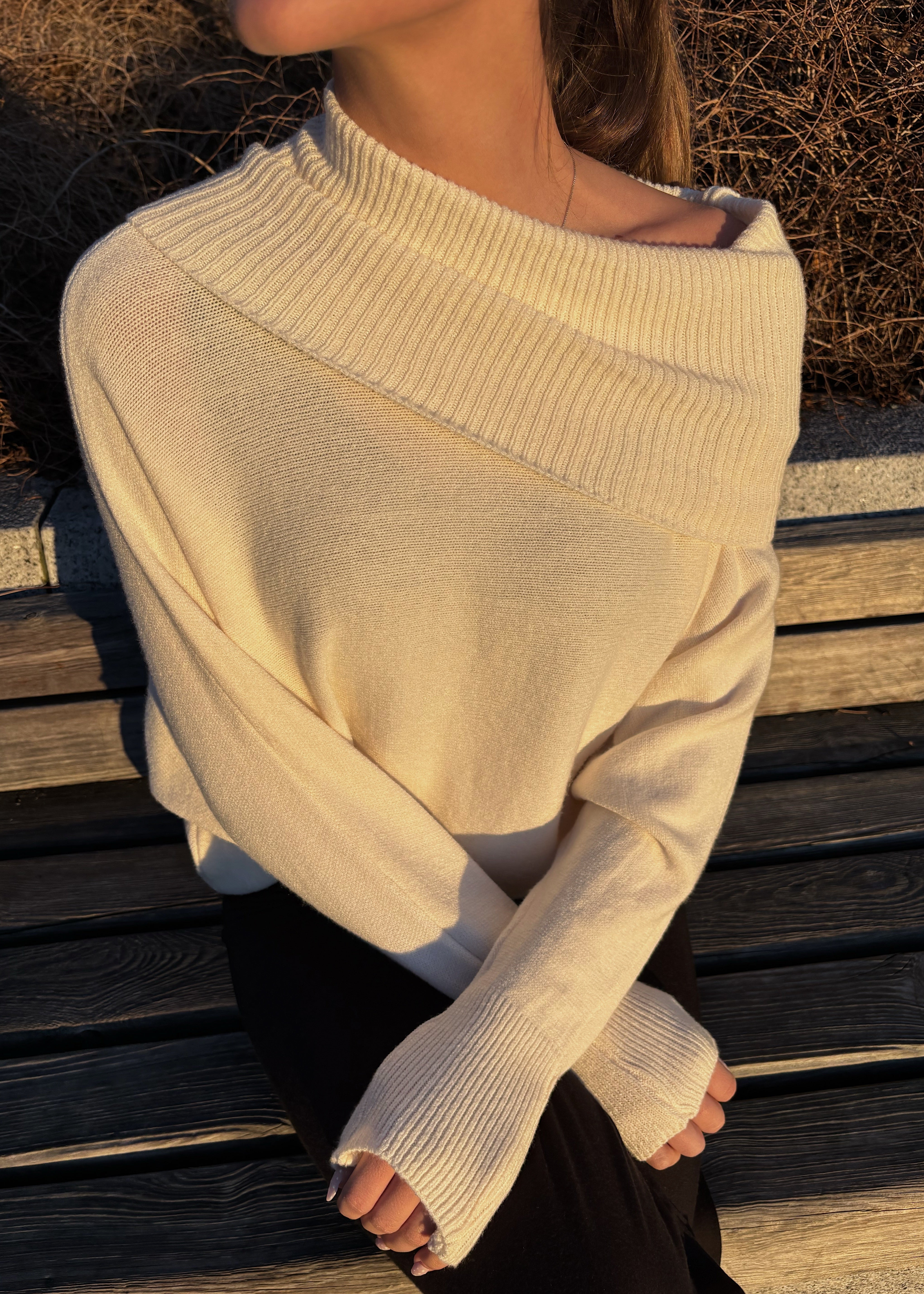 Person wearing a beige sweater sitting on wooden steps.