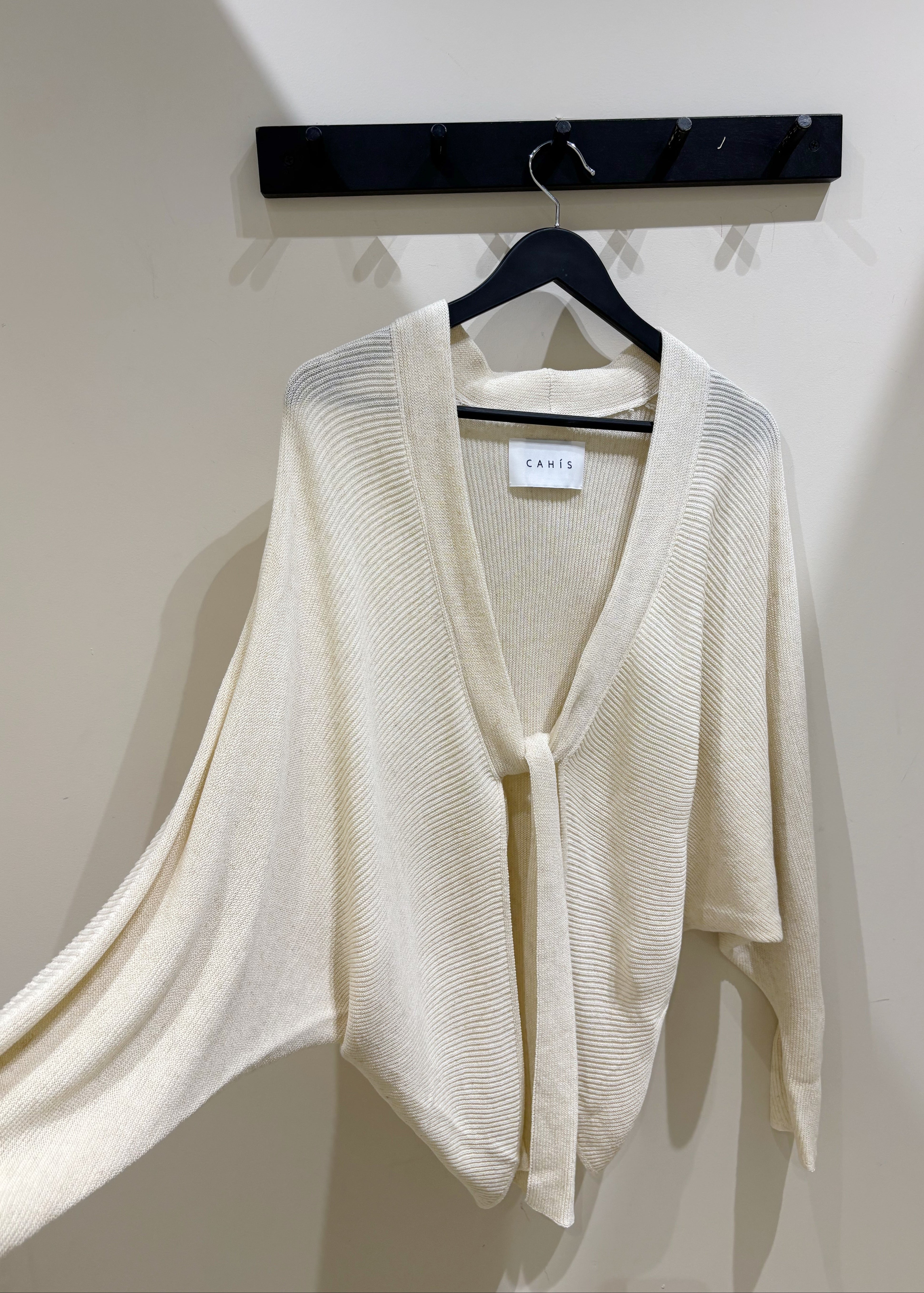 Beige cardigan on a hanger against a white wall