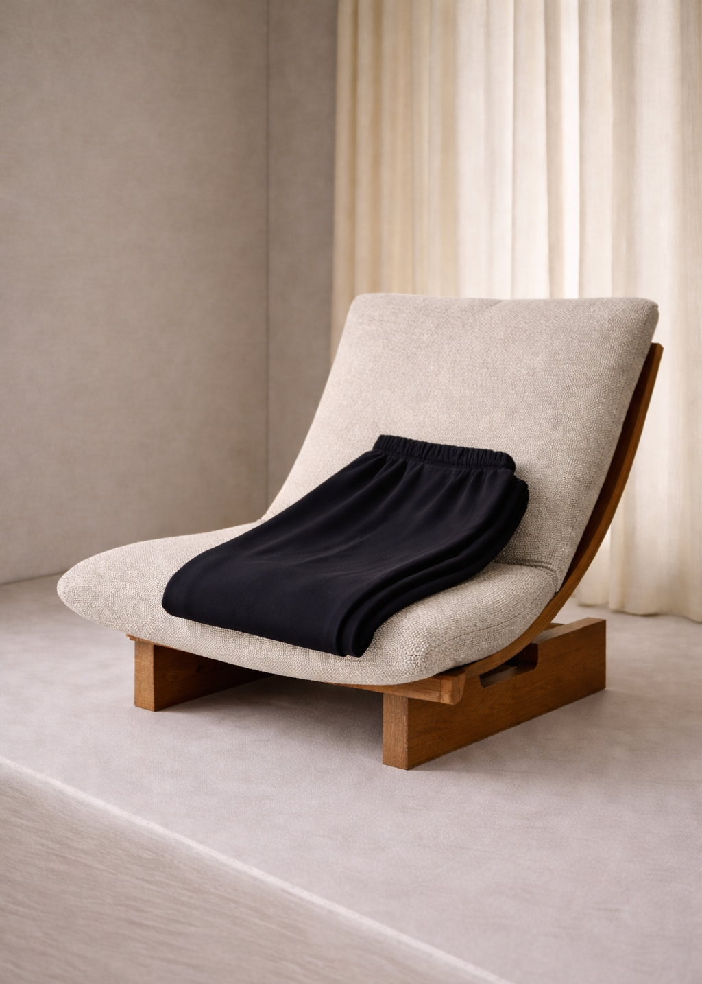 Beige lounge chair with a black blanket on a neutral background
