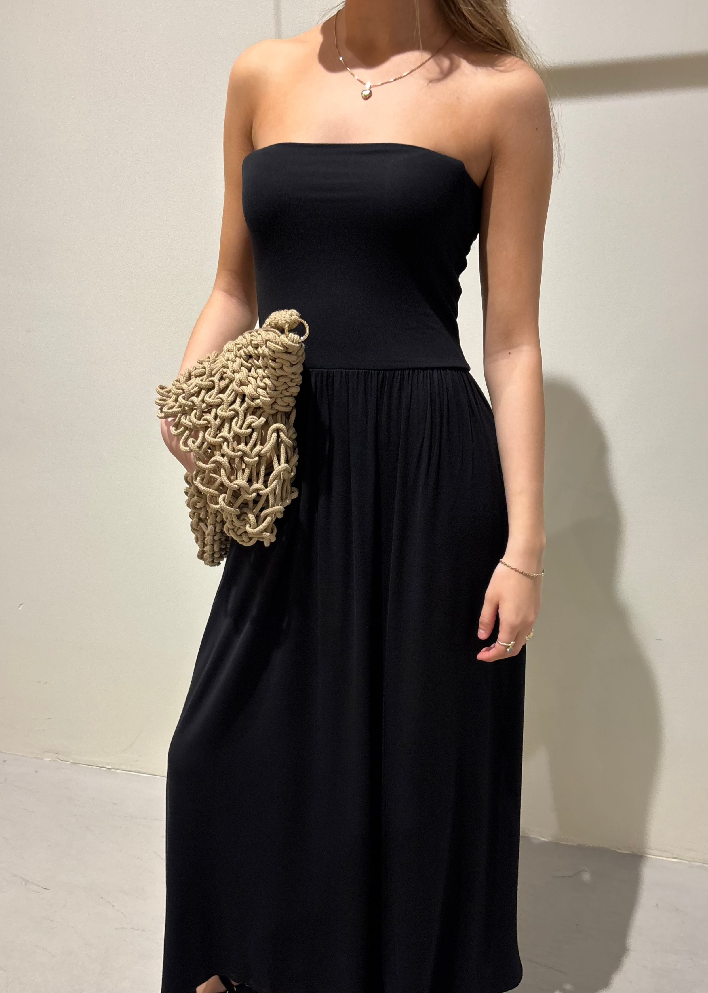Woman wearing a black strapless dress holding a textured beige clutch against a plain background