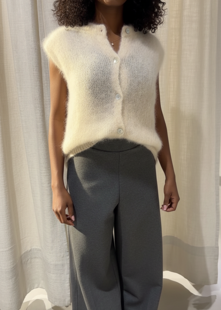Person wearing a white knitted vest and gray pants against a neutral background