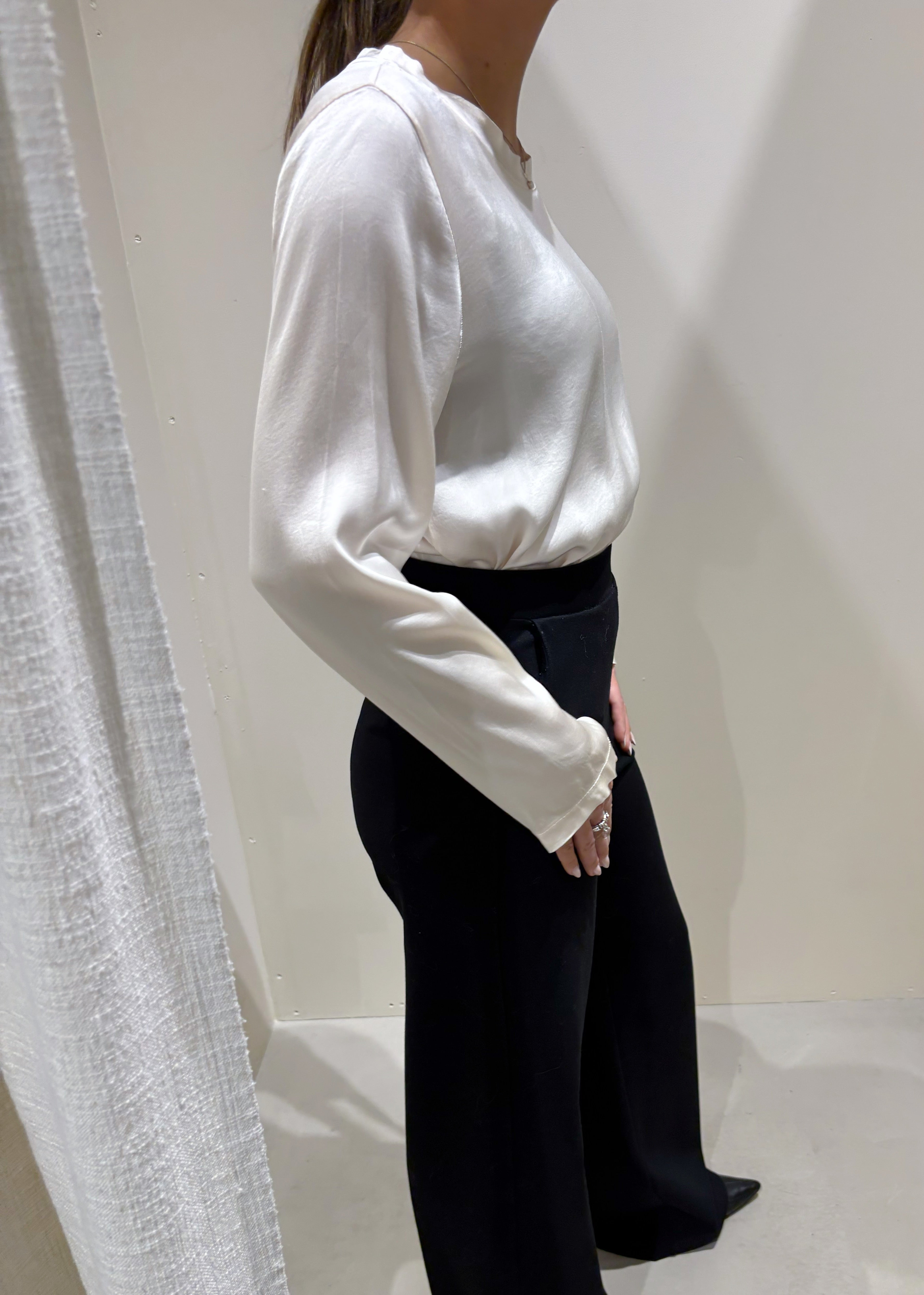 Person wearing a white blouse and black pants standing against a plain white background