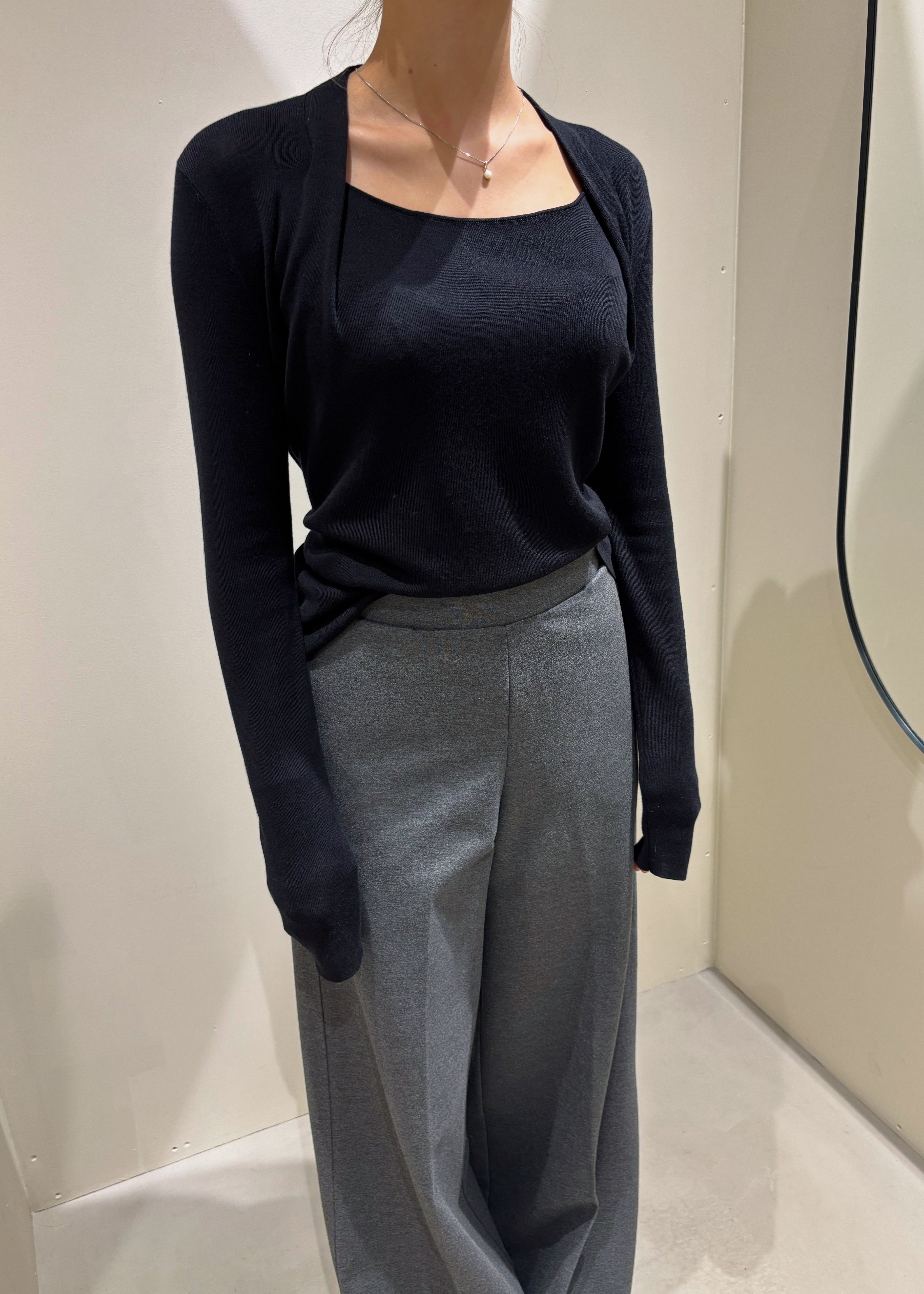 Person wearing a navy cardigan over a black top and gray pants in a neutral setting