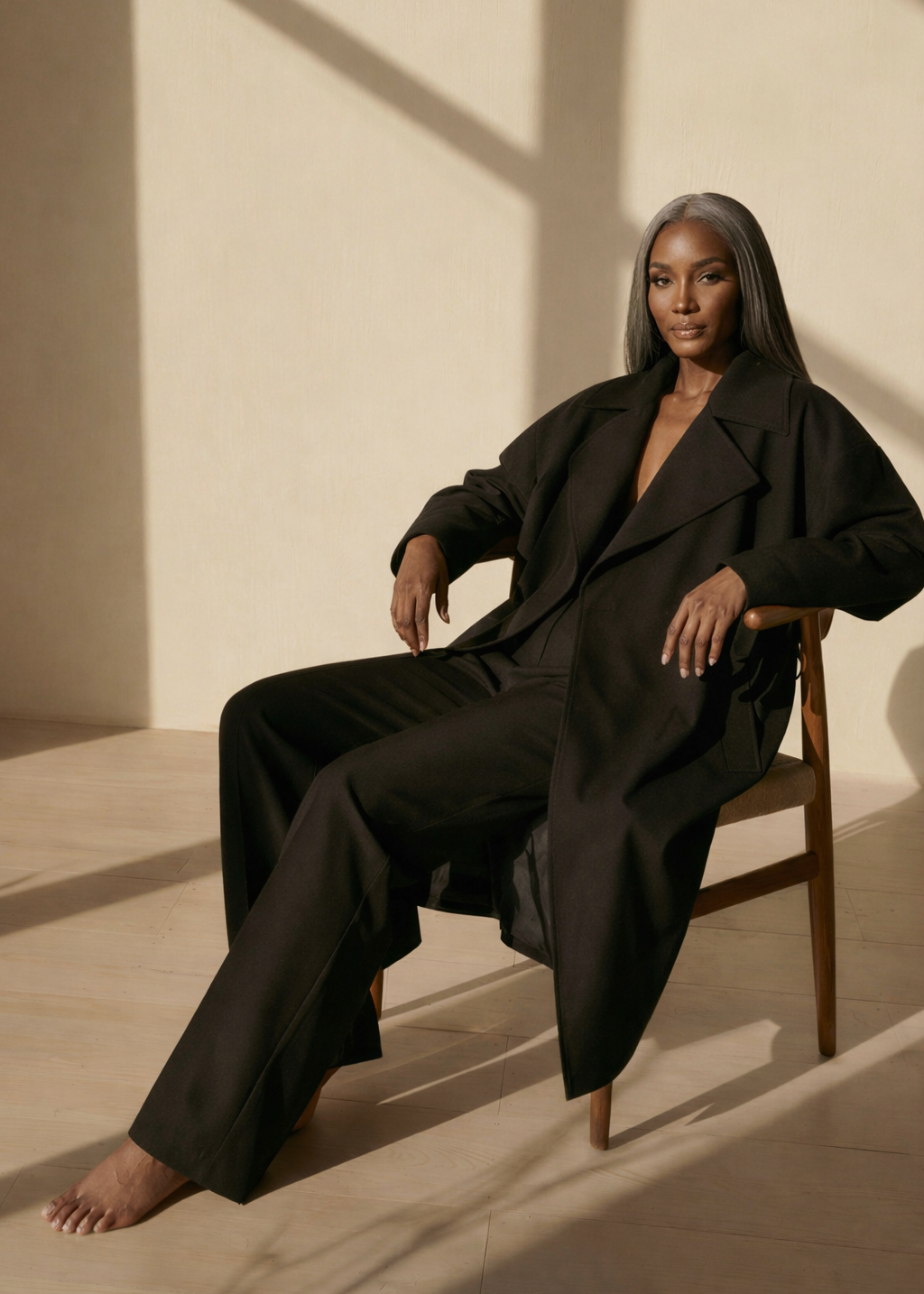 Woman in a black outfit sitting on a chair with a neutral background