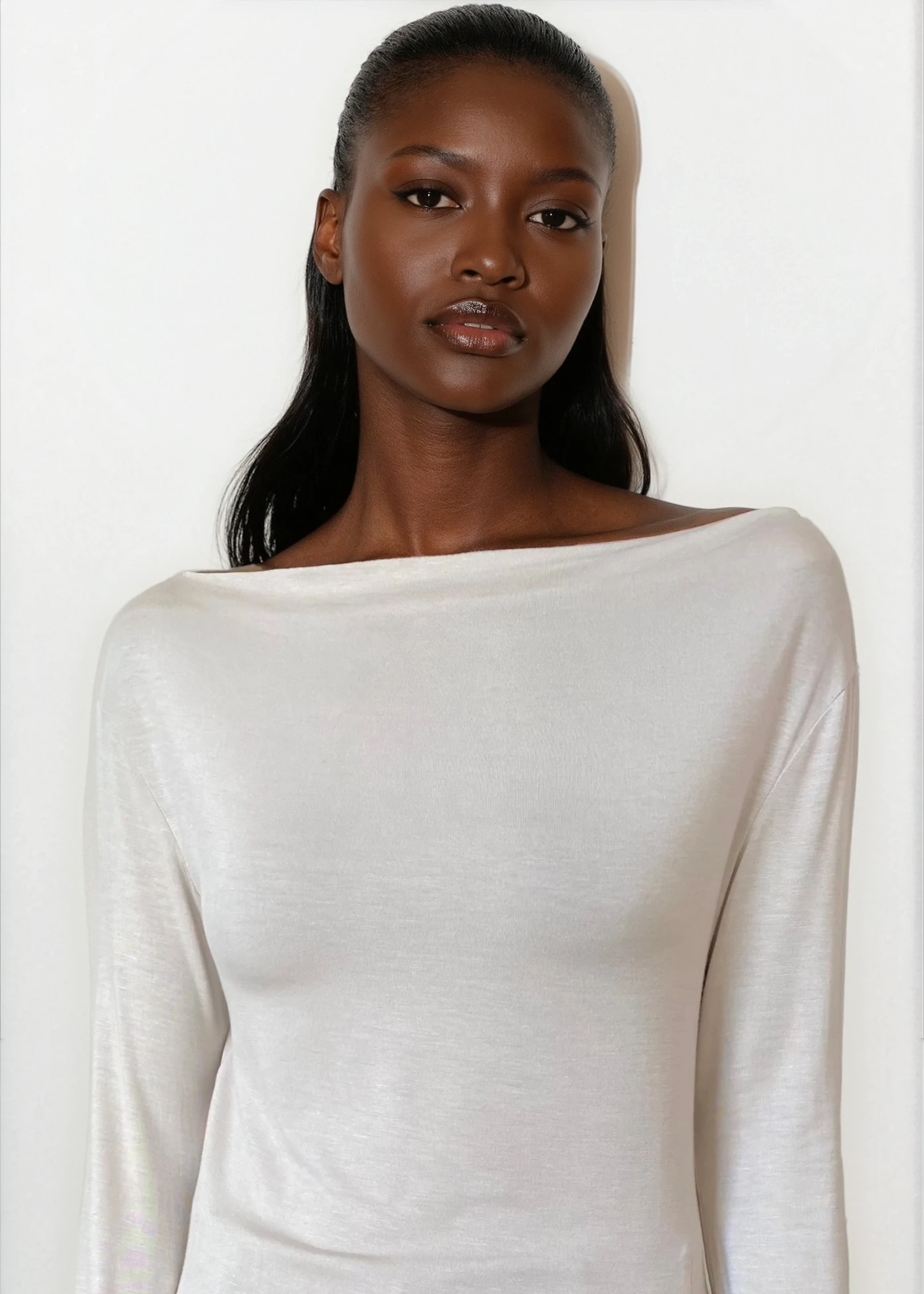 Woman wearing a white long-sleeve top and dark pants on a white background