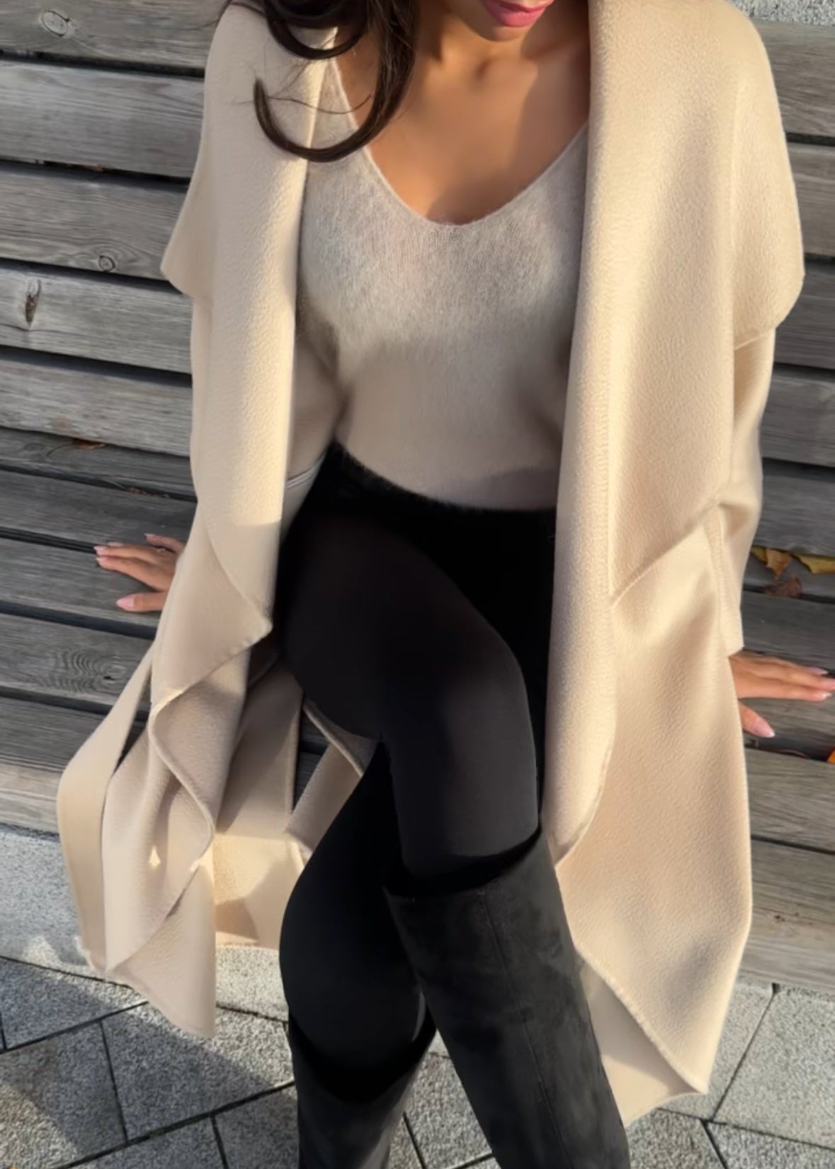 Person wearing a beige cardigan, white top, and black leggings outdoors on a wooden deck.