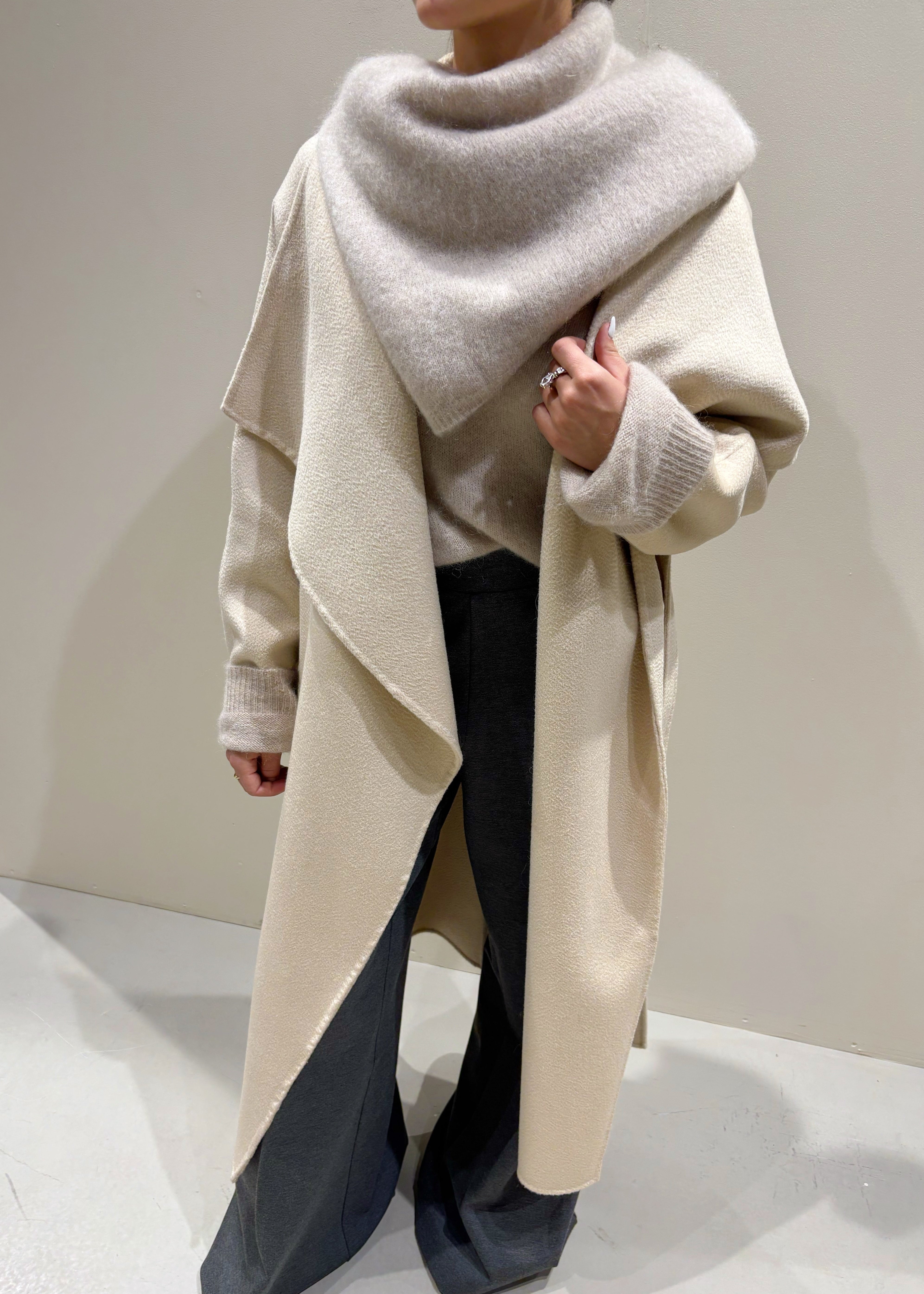 Person wearing a beige coat and gray scarf on a plain background