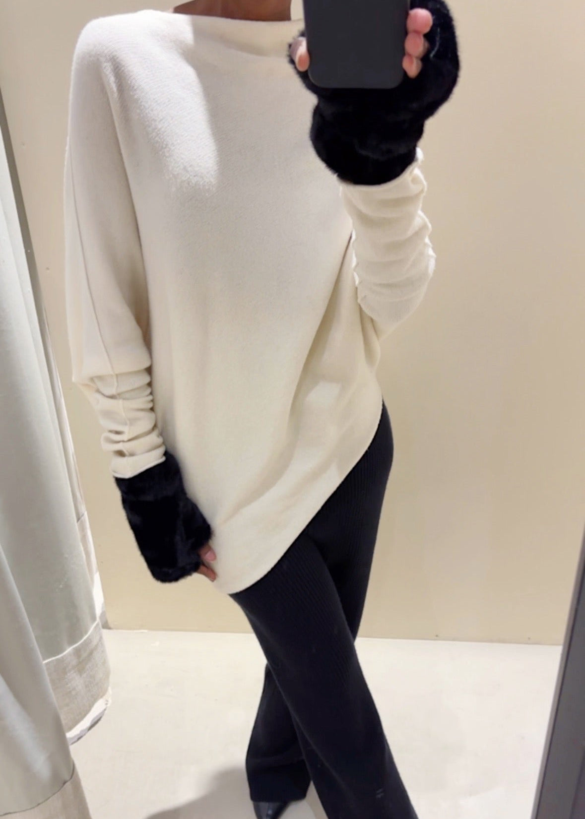 Person wearing a white sweater and black pants in a mirror reflection.