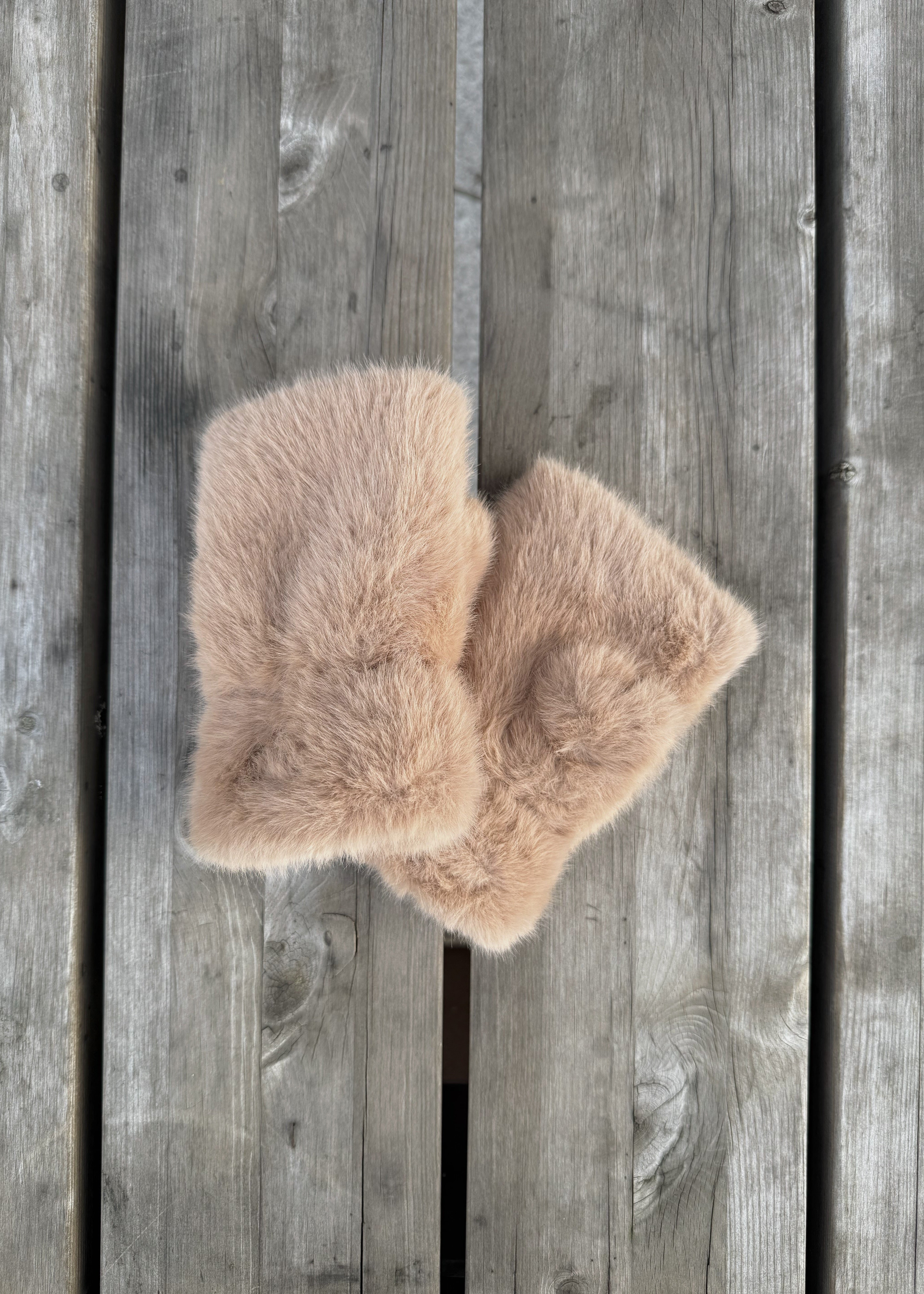 Two beige faux fur items on a wooden surface