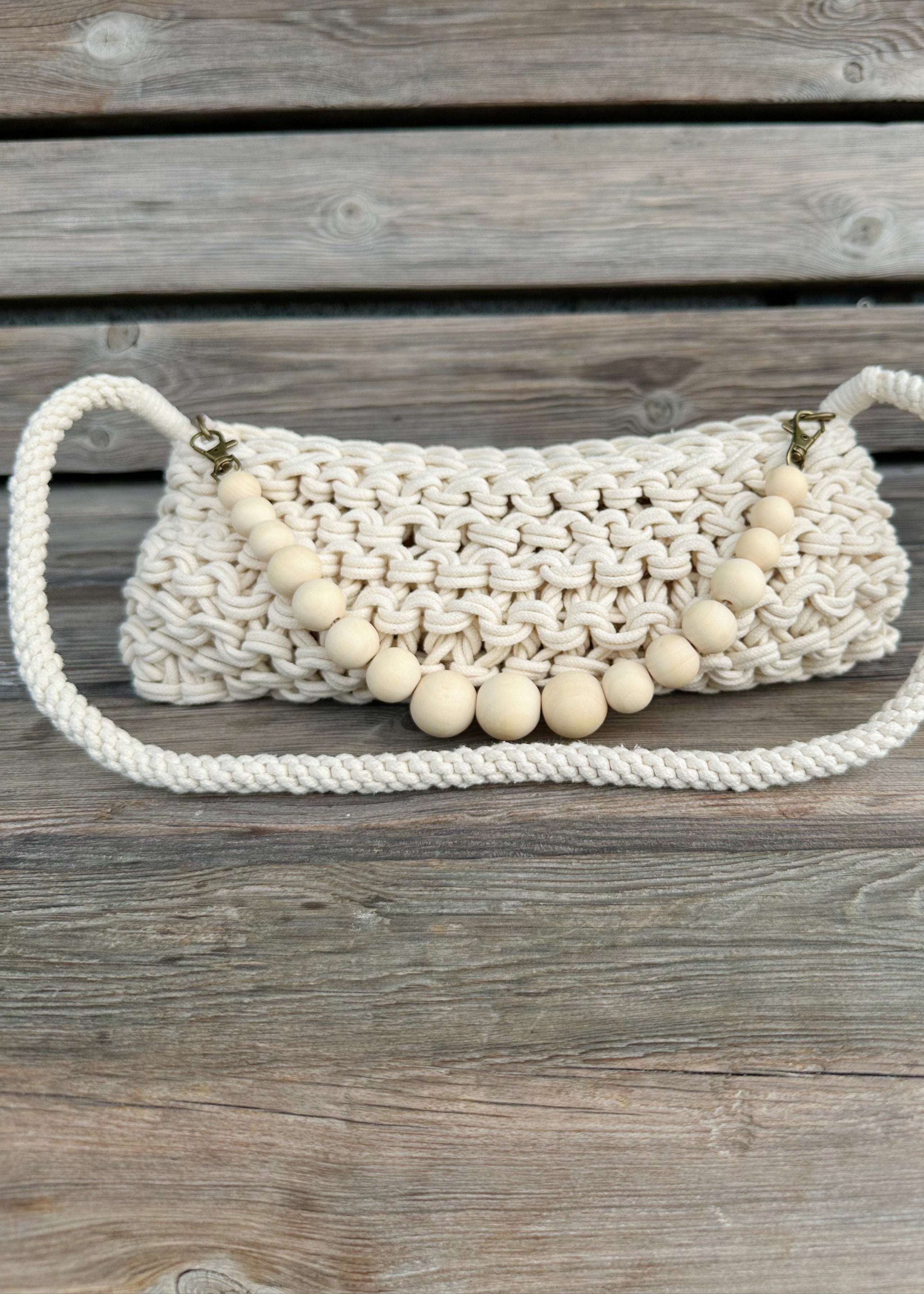 White woven handbag with wooden beads on a wooden surface