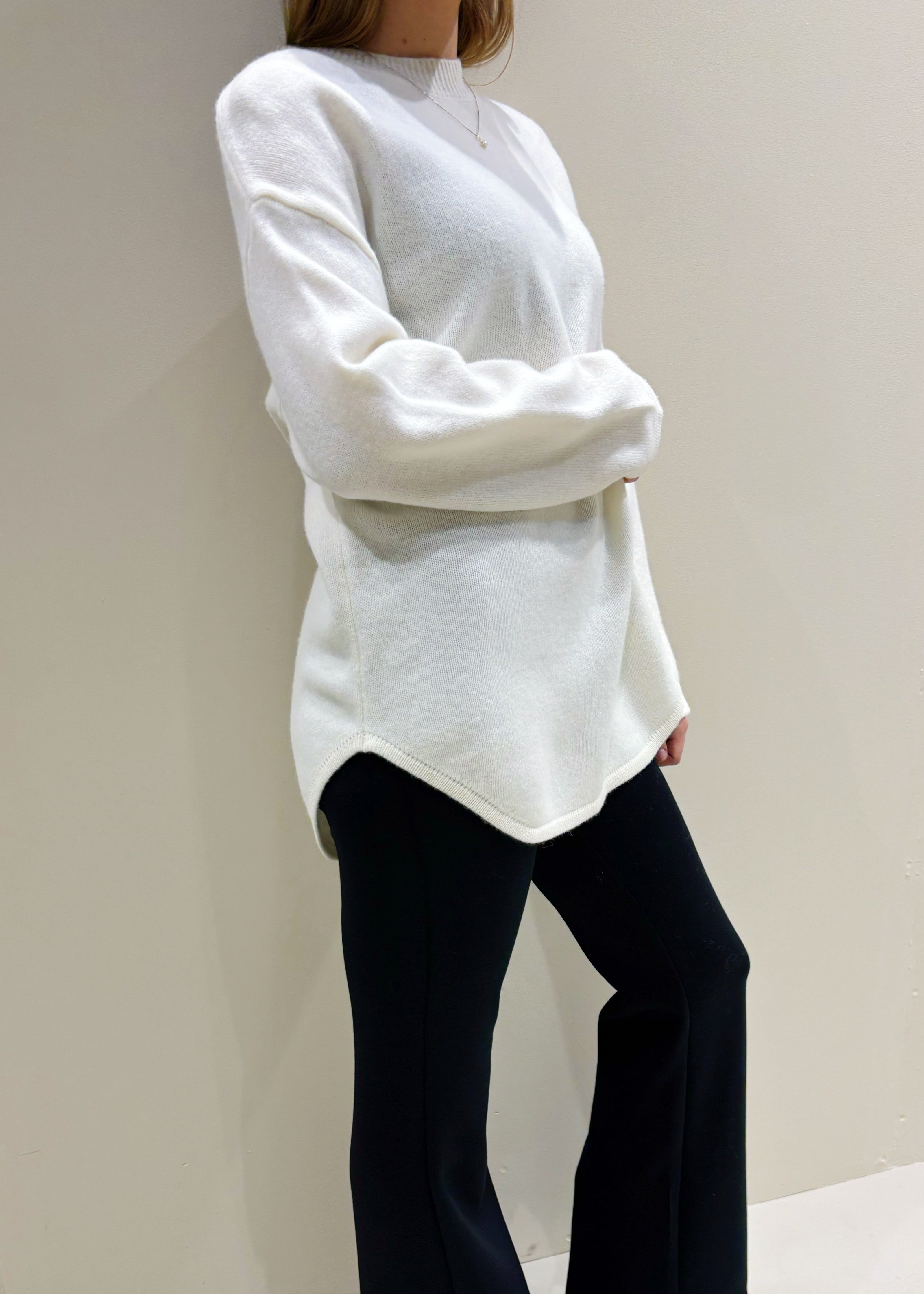 Person wearing a white sweater and black pants in a minimal indoor setting