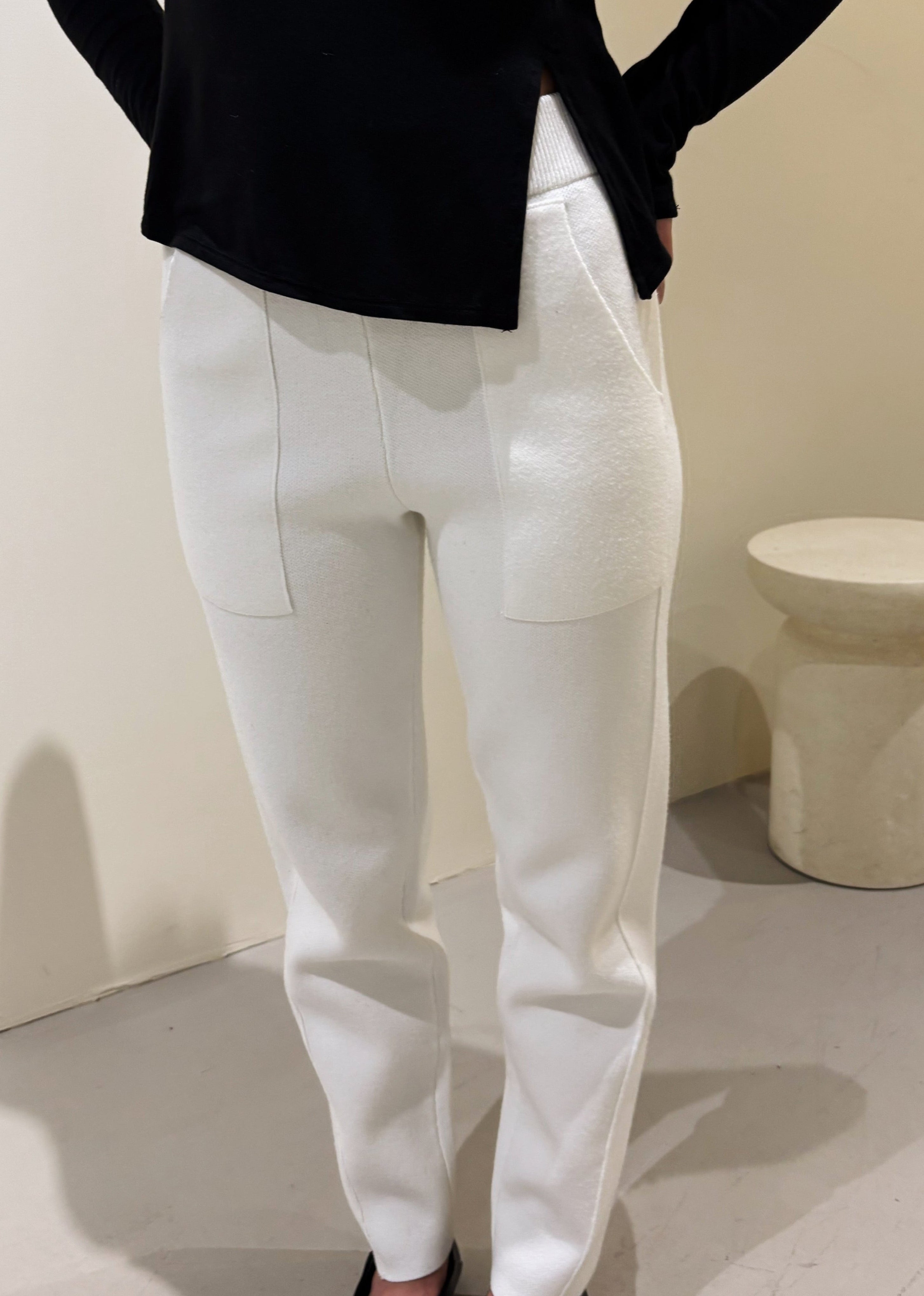 A person standing in a relaxed pose wearing white high-waisted pants with large front pockets and a black top.