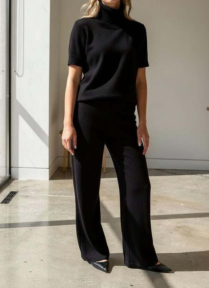 Woman wearing a black turtleneck and black pants in a minimalistic room.