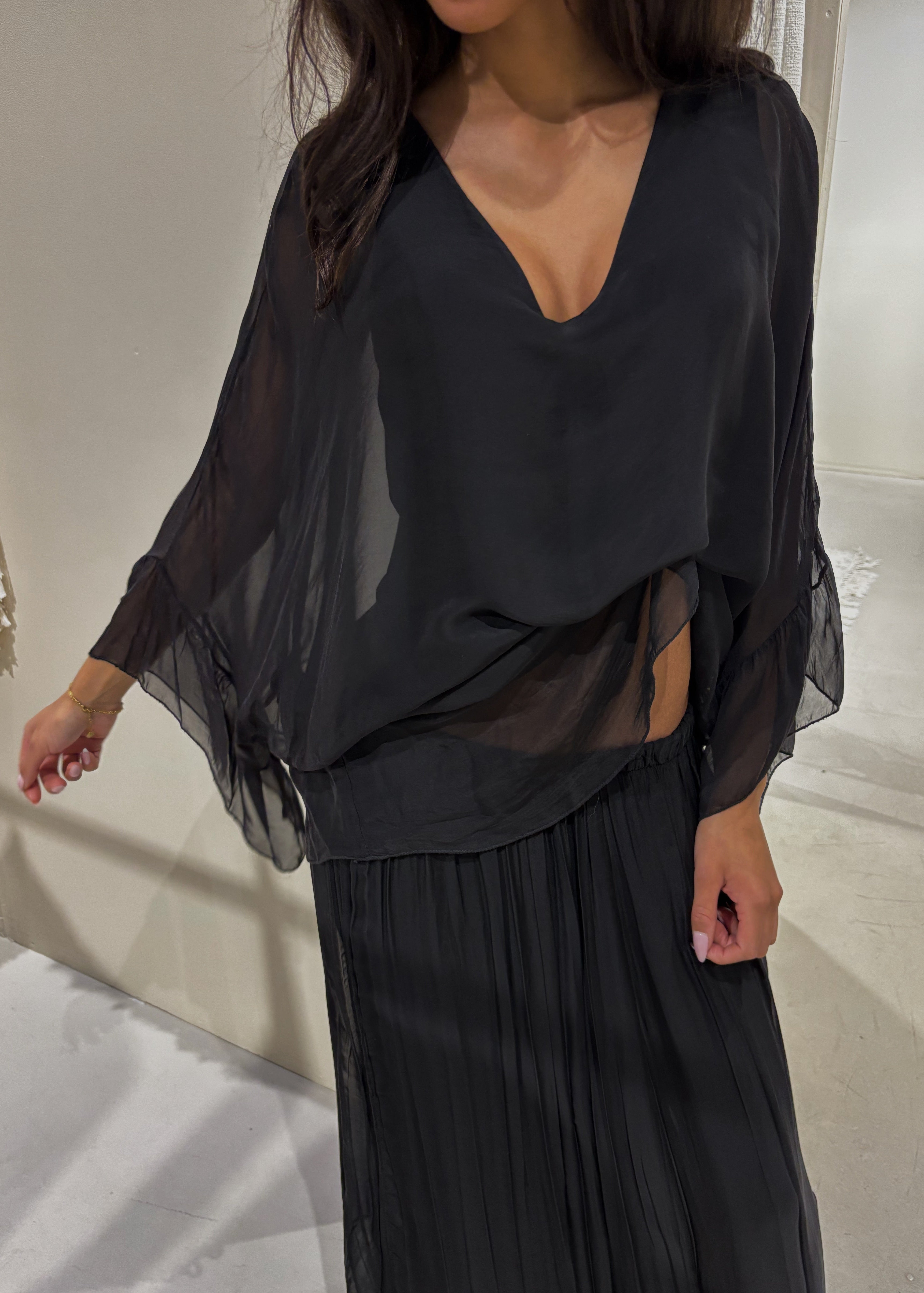 Person wearing a black outfit with sheer sleeves against a neutral background