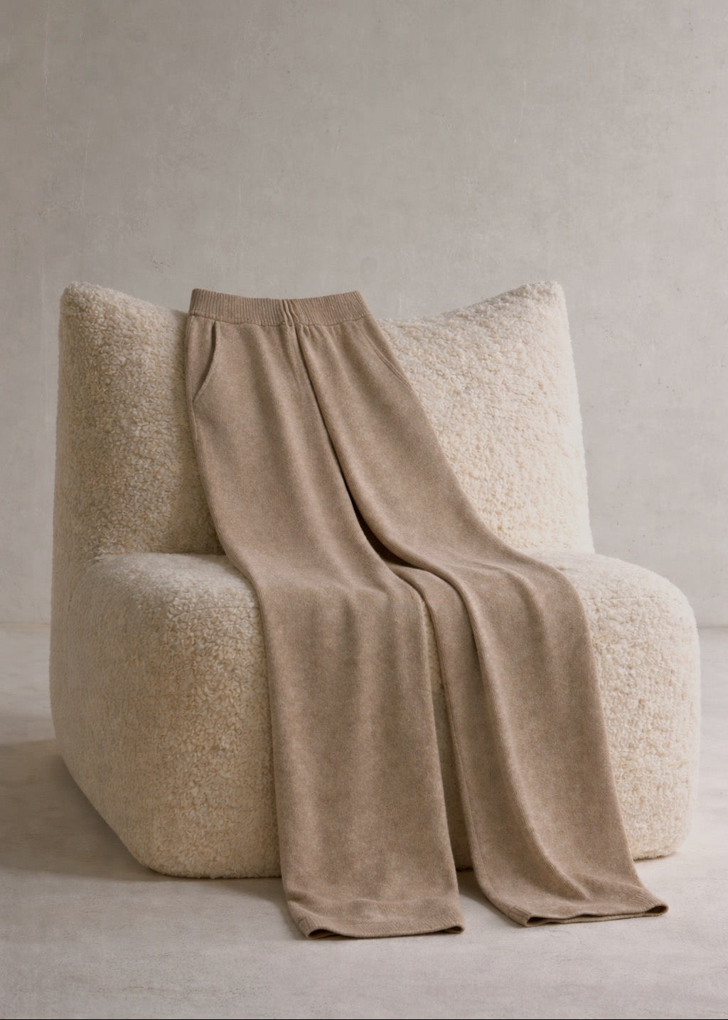 Beige pants draped over a textured chair against a plain background
