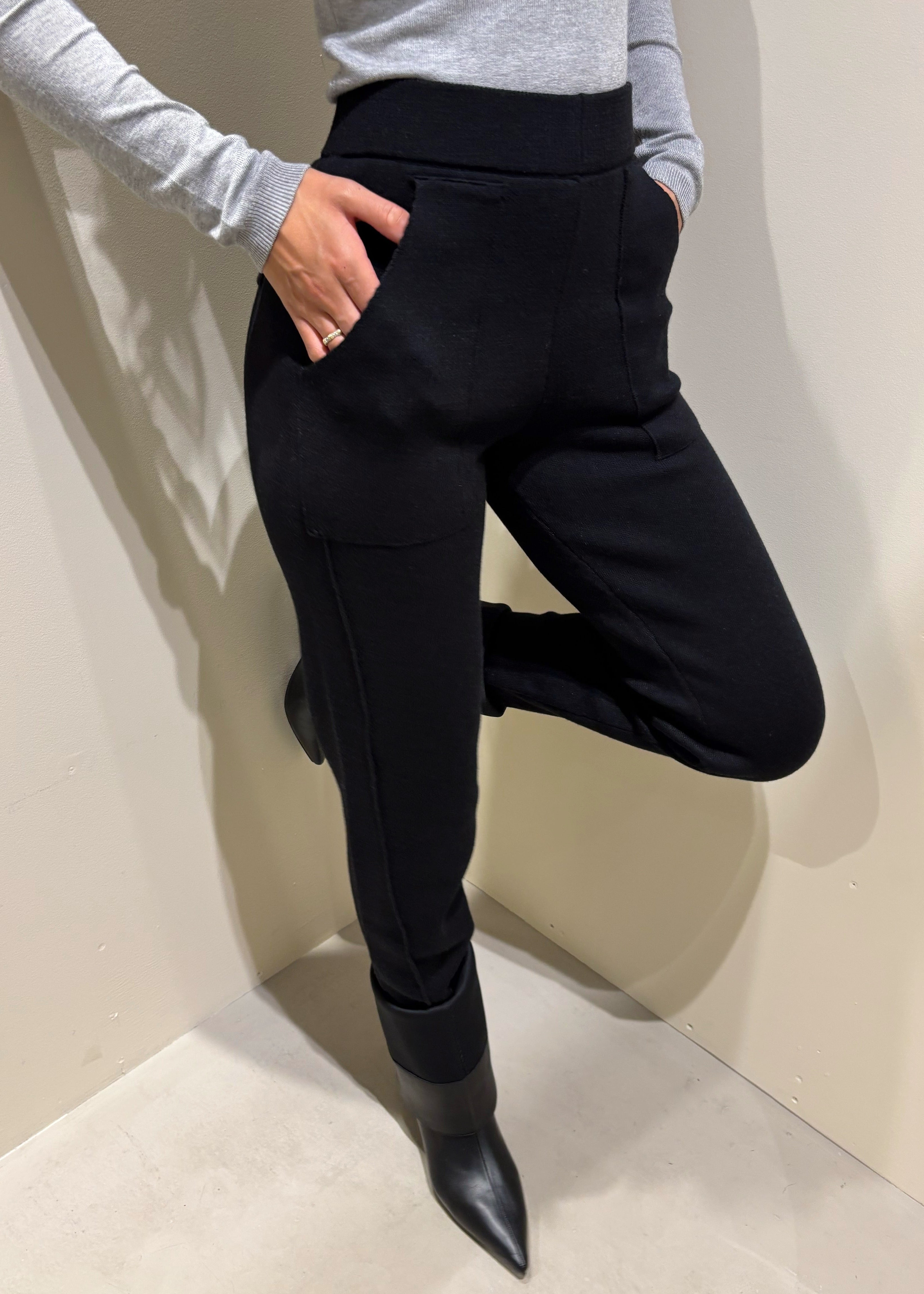 Person wearing black pants and a gray top against a plain background