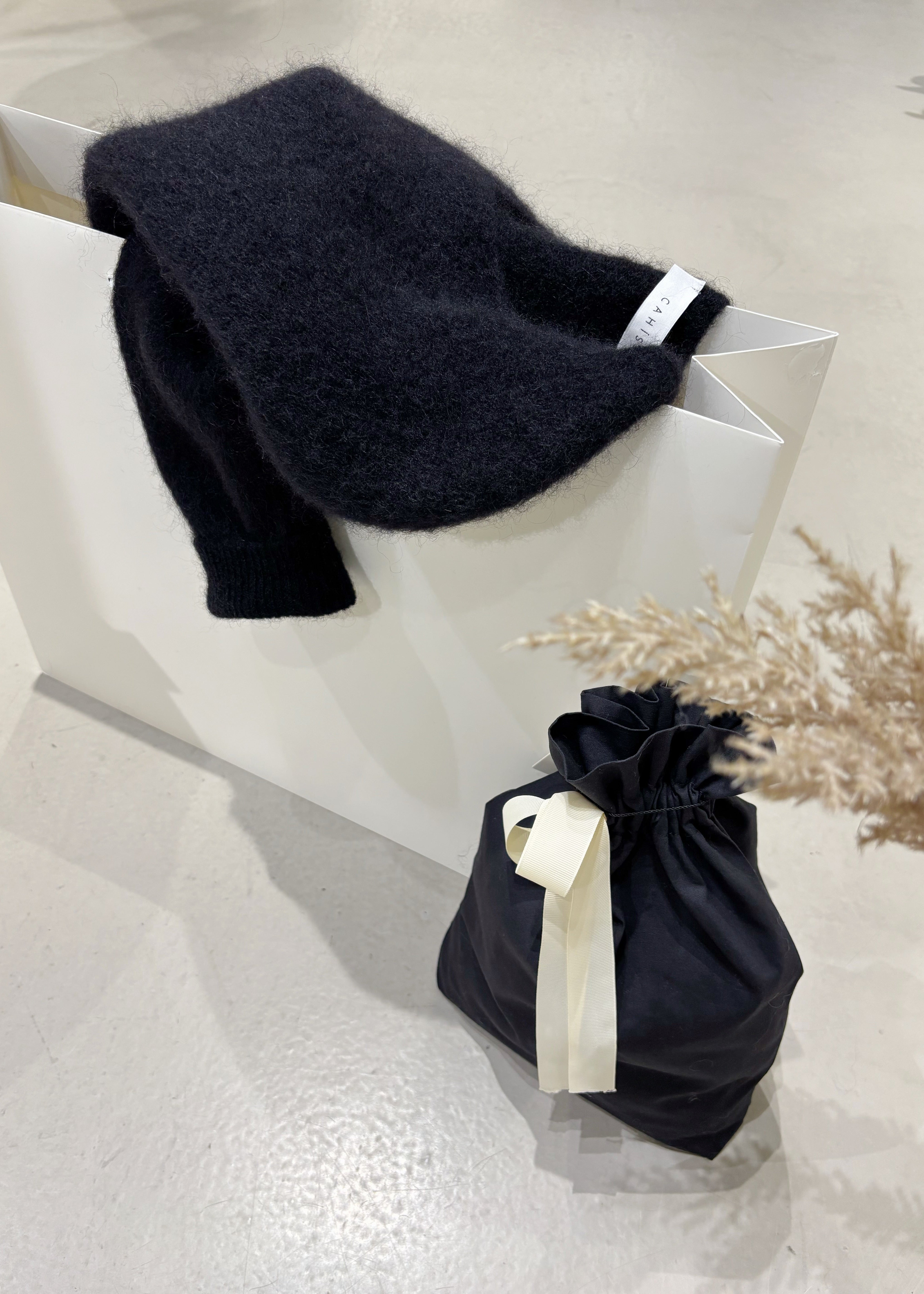 Black sweater draped over a white chair with a matching black drawstring bag on a light surface.