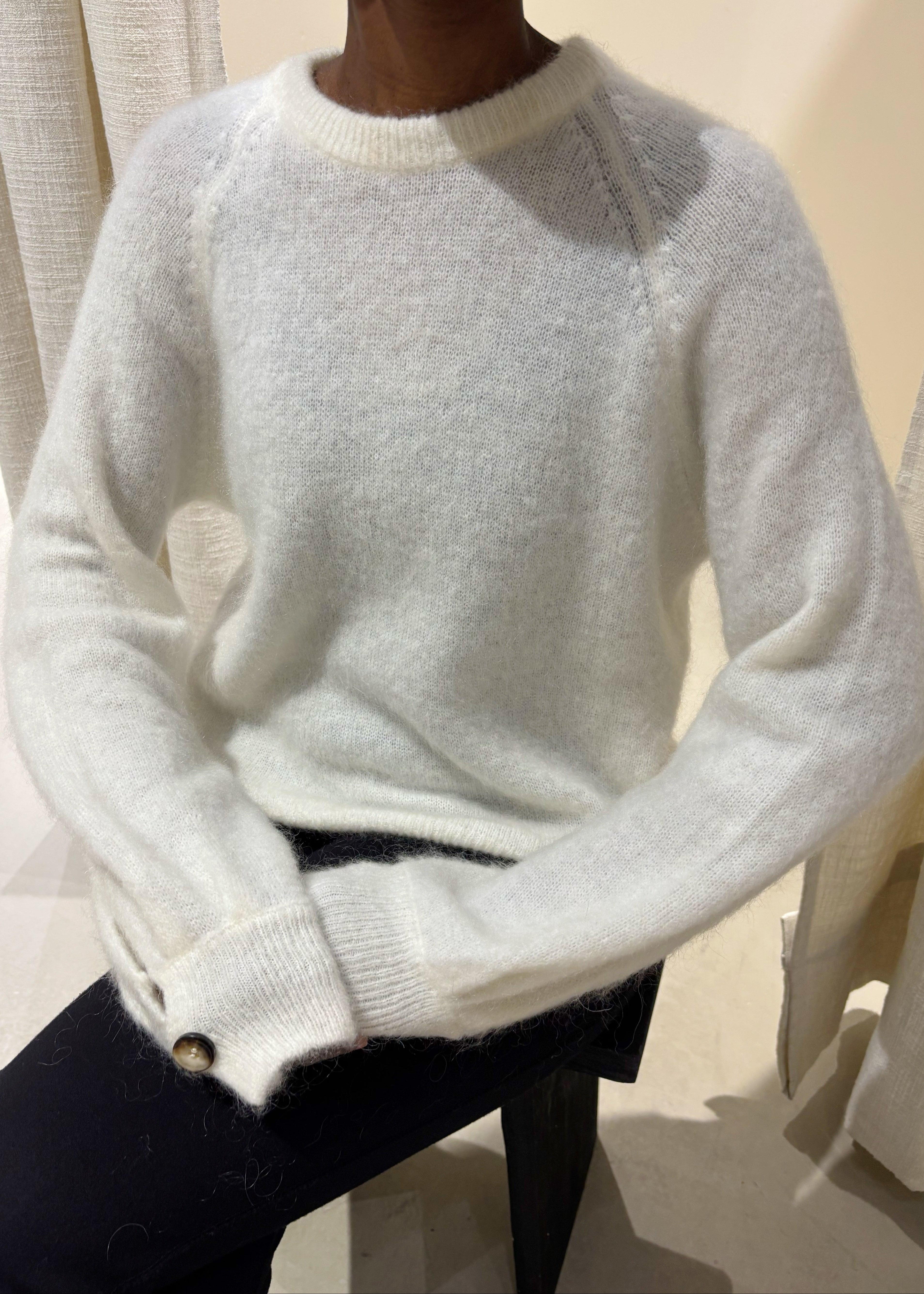 Person wearing a white sweater with a neutral background white 