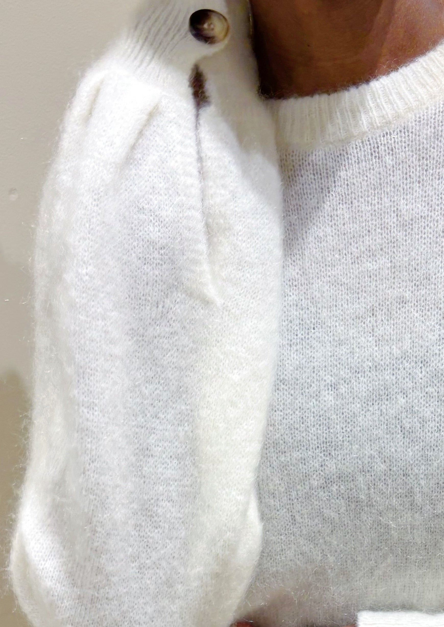 Person wearing a white sweater and dark pants against a neutral background