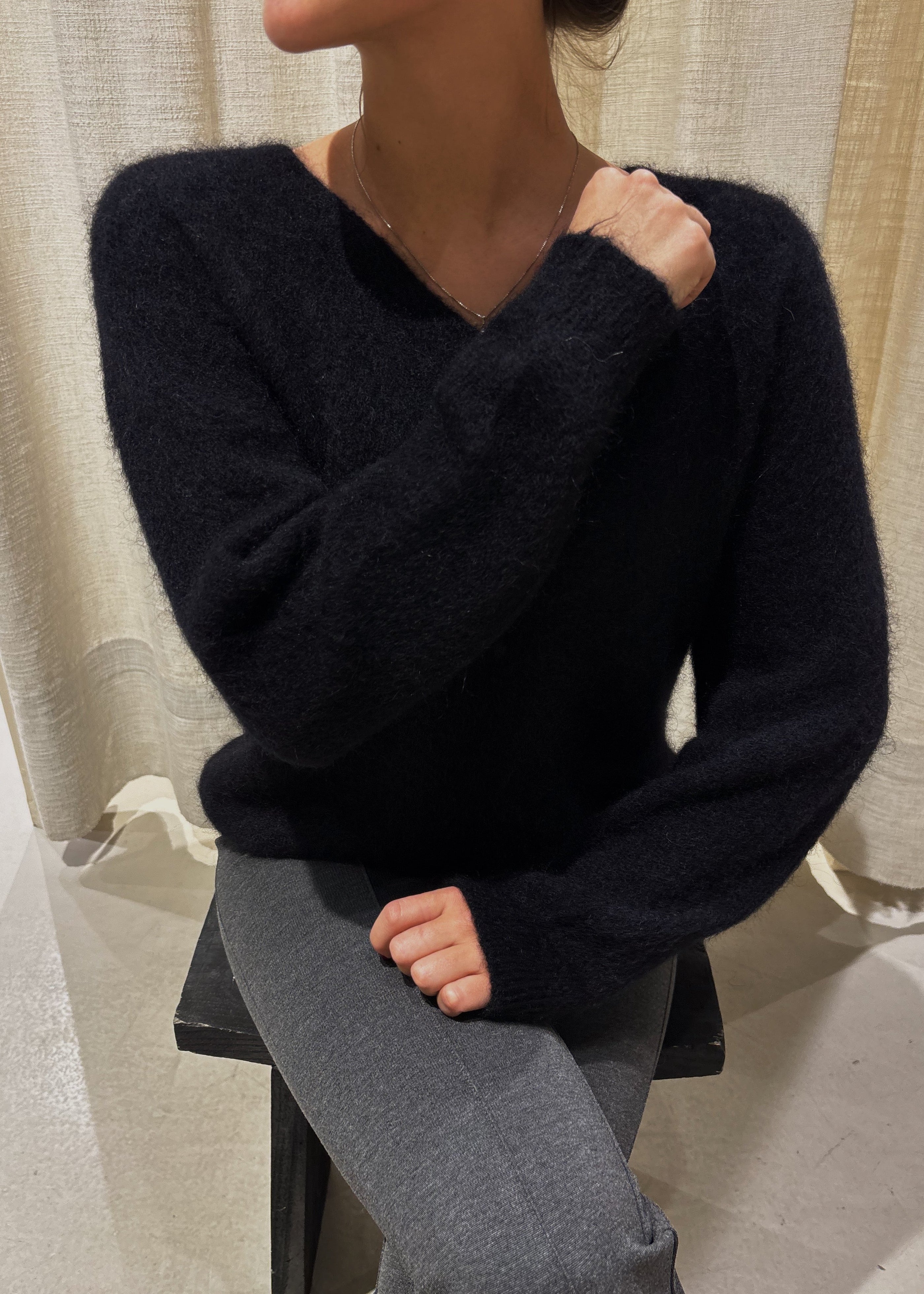 Person wearing a dark blue sweater and gray pants sitting on a chair with a neutral background
